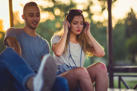 Two careless people are enjoying the sunset view in the park and listening music on headphones