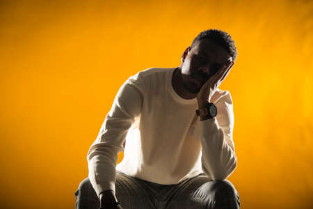 Young black male is posing with his hand on the face while sitting on the chair