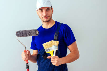 Workman standing on white background while holding brushesh for painting
