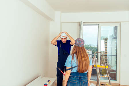 Young couple prepare to painting wall in empty room while standing in living roomの写真素材
