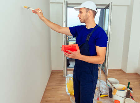 Cheerful painter in blue overall renovate his room while painting wallの写真素材
