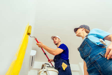 Couple wearing blue overalls painting their living room in yellow colorの写真素材