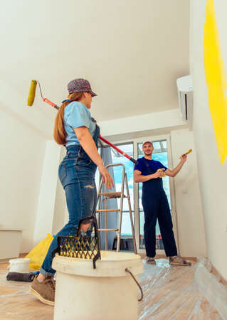 Beautiful woman painting room yellow with paint stick roller in their new houseの写真素材