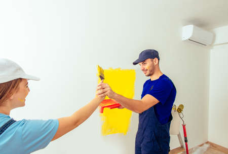 Two people palying with paintbrush and having fun while coloring walls