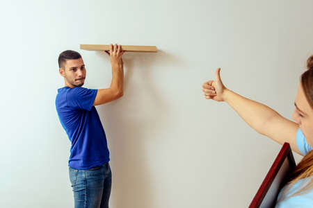 Young woman showing to boyfriend for hanging shelf on wall at homeの写真素材