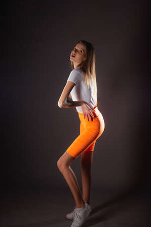 Pretty sports girl with short orange leggings posing isolated on dark background in studioの写真素材