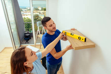 Man and woman putting shelf on the wall at home