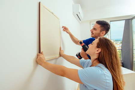 Couple is doing repair and hanging picture on the wall at homeの写真素材