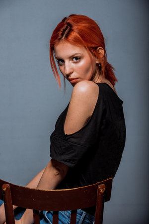 Body shot of a cool young woman wearing modern style black top sitting on cheirの写真素材