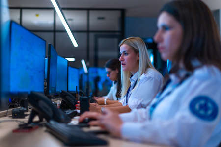 Happy security data center operator colleagues (coworkers) smiling and monitoring the CCTV footage while typing on a keyboard.の写真素材