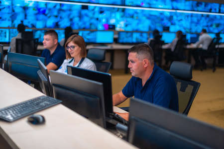 Group of Security data center operators (administrators) working in a group at a CCTV monitoring room while looking at multiple monitors ( computer screens)の写真素材