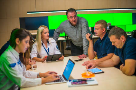 Security guard monitoring modern CCTV cameras in a surveillance room. Group of security guards sitting and having conversation.の写真素材