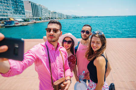 Couple of tourists is exploring new city together. Smiling and takeing a selfie, next to the sea.