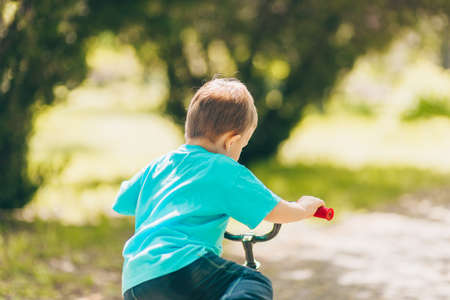 Little kid boy riding with his first bike in the city park