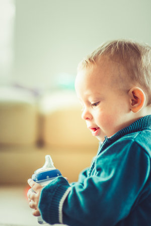 Smiling baby boy is looking curious while holding his bottle