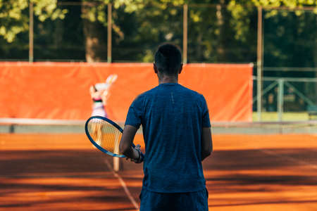 Rearview of a tennis player ready to serve on a clay court wearing blue sportswearの写真素材