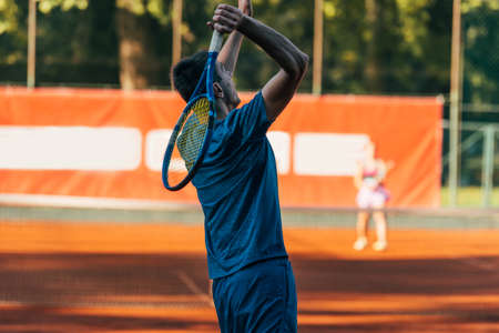 Rearview of a tennis player ready to serve on a clay court wearing blue sportswearの写真素材