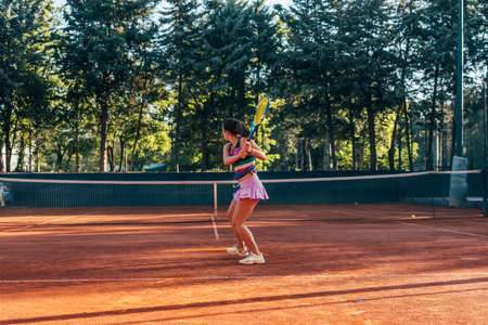 View from the back of a young female paying tennis on a court outsideの写真素材