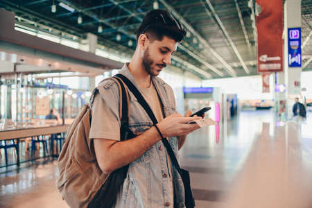 Portrait of a happy young man with traveling bag looking at cell phoneの写真素材