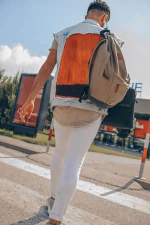 Stylish man with backpak and laptopcase while going to airport building