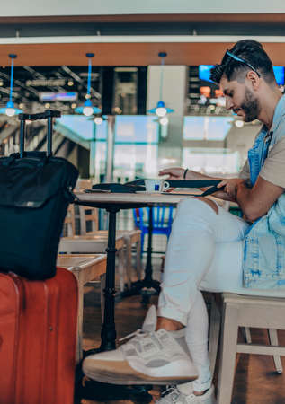 Cheerful mansitting in coffee shop at airport station while sitting near luggage