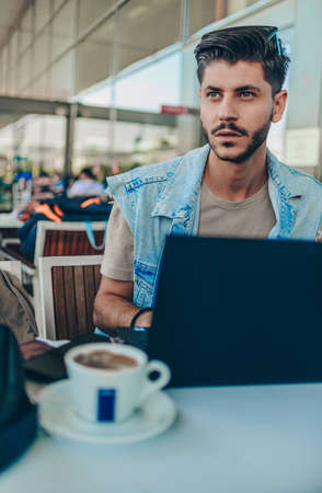 Handsome man looking at laptop while sitting in waiting hall and drink coffeeの写真素材
