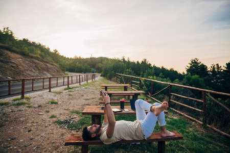 Young handsome business man lying at the bench in the hill and doing selfie