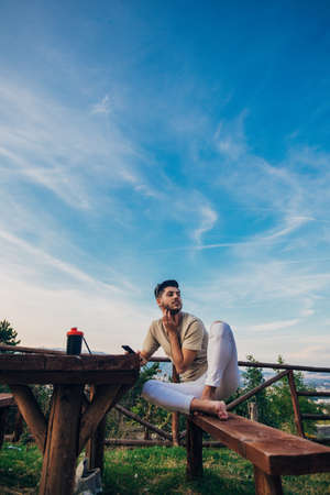Profile of a happy guy using a smart phone sitting on a bench in a park