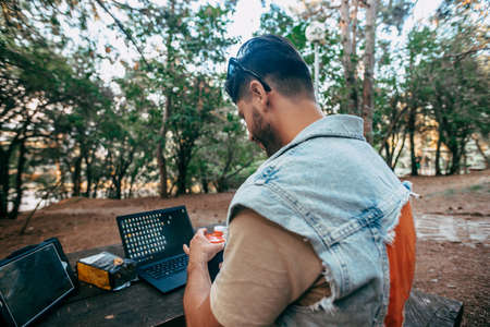 Man sitting on wooden table using laptop and digital tablet while working at the park