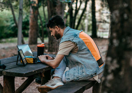 Handsome freelancer in casual outfit working with laptopand tablet at table in parkの写真素材