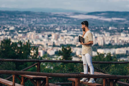 Young freelancer entrepreneur working online with a laptop  while standing on the hill and talk on...