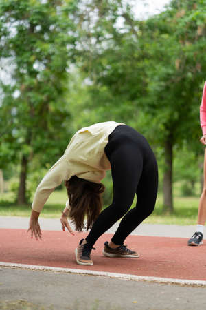 One attractive girl is bending her back while the other one is looking at her
