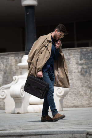 Urban and handsome businessman is talking on the phone while walking towards his company