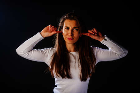Girl in her mid 20's covering ears, suffering from loud noise, unhappy female feeling pain