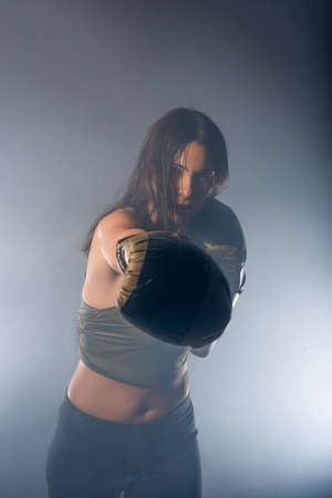 Foggy image of a young and sexy female boxer punching direct hit with boxing glovesの写真素材