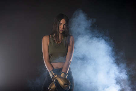 Closeup portrait of a female boxer posing with boxing gloves and looking at the camera with a smokey backgroundの写真素材