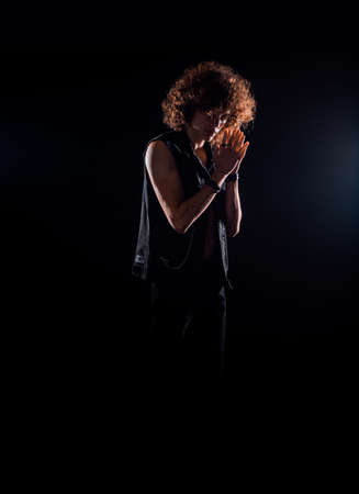 Handsome young boy wearing hipster jeans vest while posing against dark background