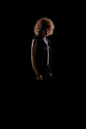 Cool handsome trendy guy wearing stylish jeans vest and black jeans isolated on black wallの写真素材