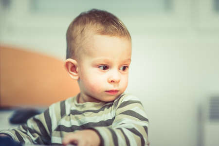 A cute little baby is looking serious while standing in the roomの写真素材