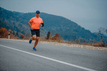 Middle aged man in good shape jogging on a concrete road surrounded by natureの写真素材