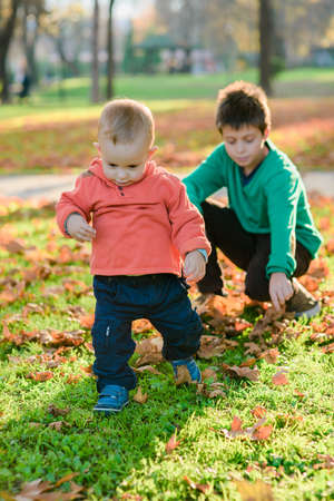 Older and little brothers having fun while hug each other in the autumn park