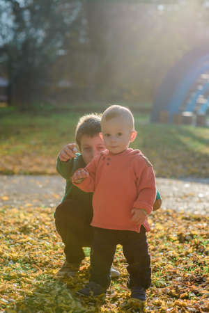 Small cheerful kids playing in the park while standing on golden leavesの写真素材