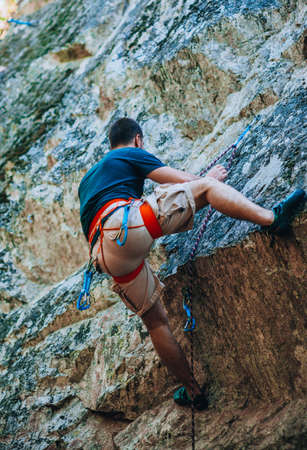 Young fearless man climbing a steep wall in mountainの写真素材