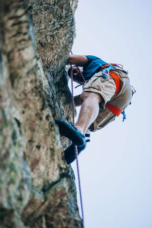 Young man climbing on a wall with blue sky on the backgroundの写真素材