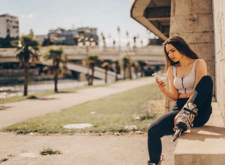 Cute girl with roller skates is sitting in the city and  looking at her phone