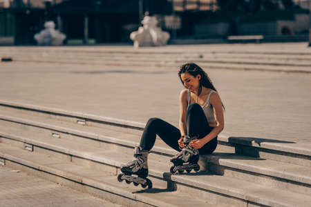 Pretty Hispanic young woman putting her inline skates on and smilingの写真素材