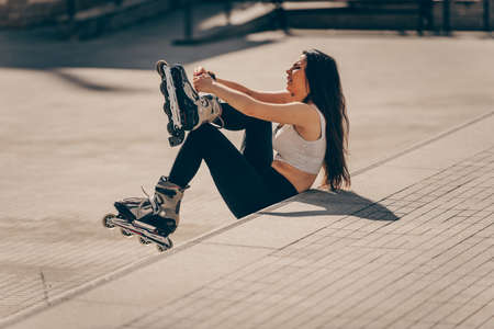 Young woman taking on roller skates while sitting on wallの写真素材