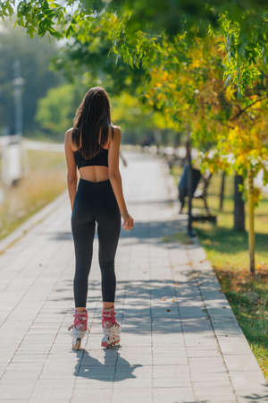 Rearview of young fit female on roller skates riding outdoors on urban street in the park.の写真素材