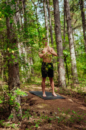 Image of a handsome cheerful young sports fitness man standing in green park nature make sport exercises for legs squatsの写真素材