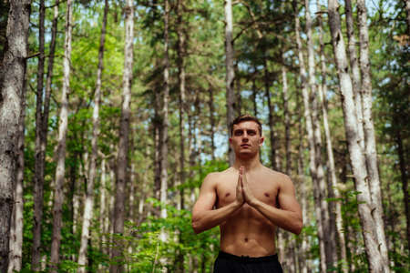 A sporty man with a muscular body doing exercises on a meadow on a natural background. Sports and yoga conceptの写真素材